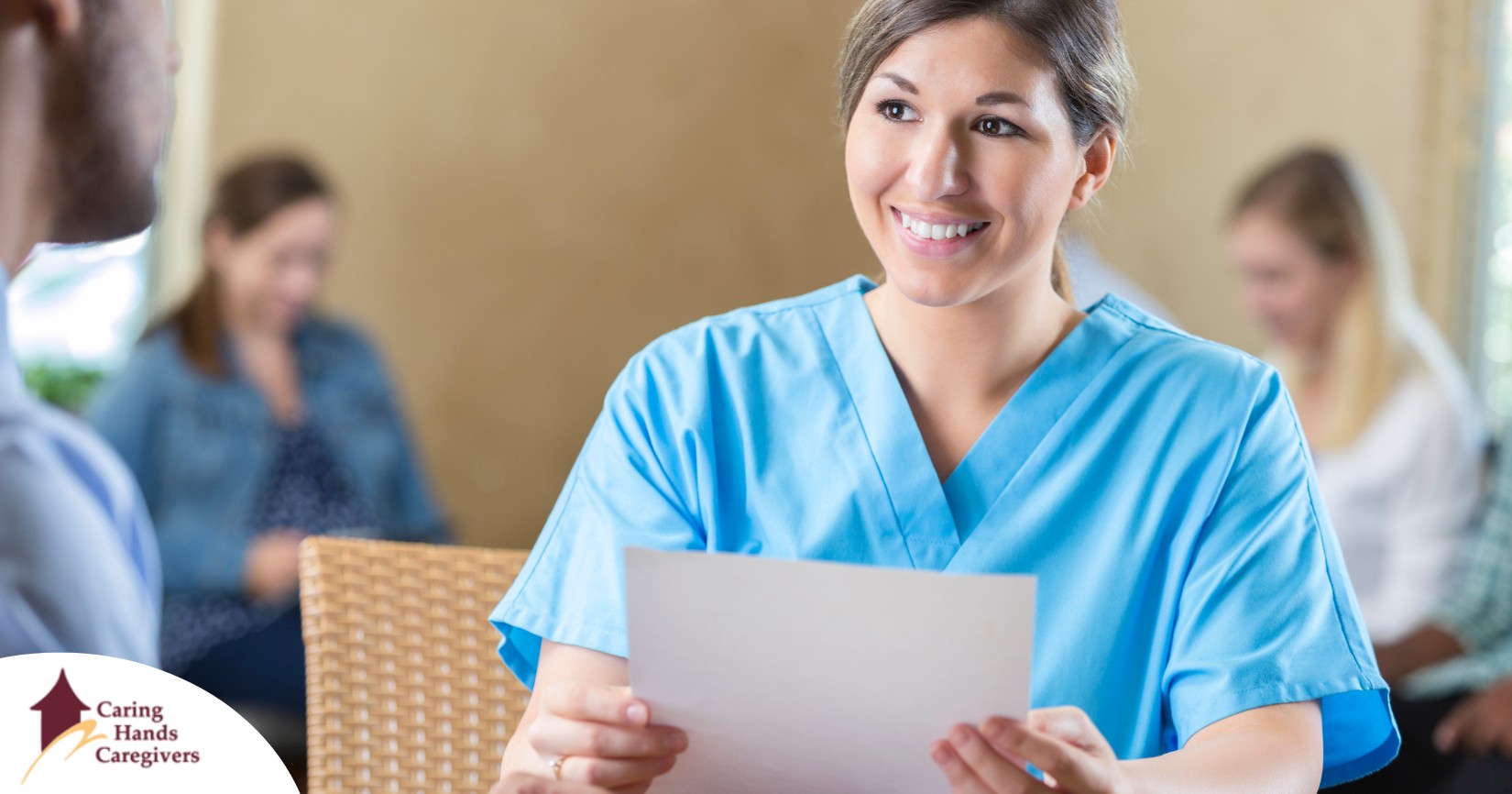 A woman in scrubs holds a paper while interviewing with someone else, representing how a solid caregiver resume can get you to an interview.