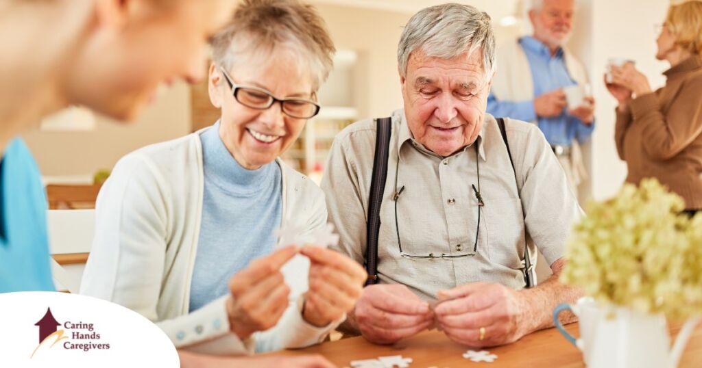 An older couple works on a puzzle with a caregiver, representing the kind of activity that helps those with dementia and also representing Alzheimer’s and Brain Awareness Month.