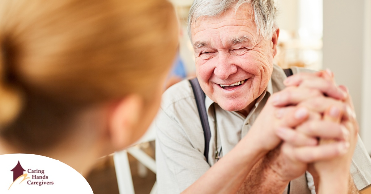 A caregiver holds hands with a happy older client, representing the results of creating a comfortable environment in the home.