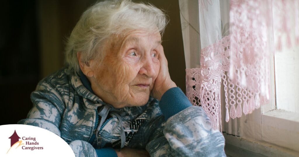 An older woman peacefully looks out of the window while the sun is still up, representing what can happen with sundowning.