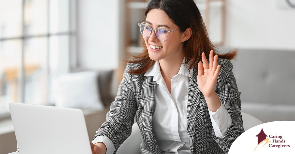 A well-dressed woman smiles and says hi on a videoconference, representing a candidate who is well-prepared for a caregiver interview.