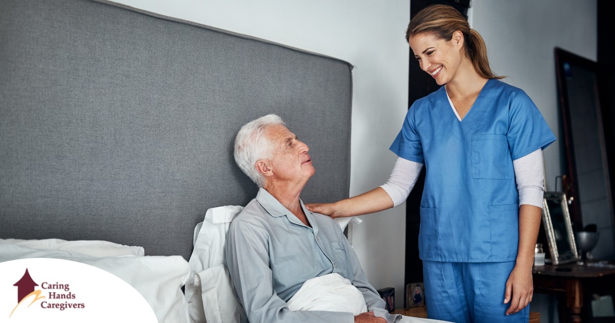 A caregiver smiles at an older client in bed, representing the compassion involved in being a live-in caregiver.