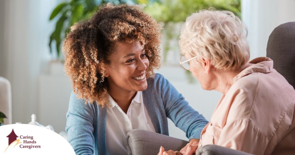 A caregiver smiles at an older client in a chair, representing the joy that can come from a healthy work-life balance.