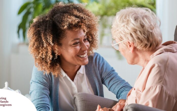 A caregiver smiles at an older client in a chair, representing the joy that can come from a healthy work-life balance.