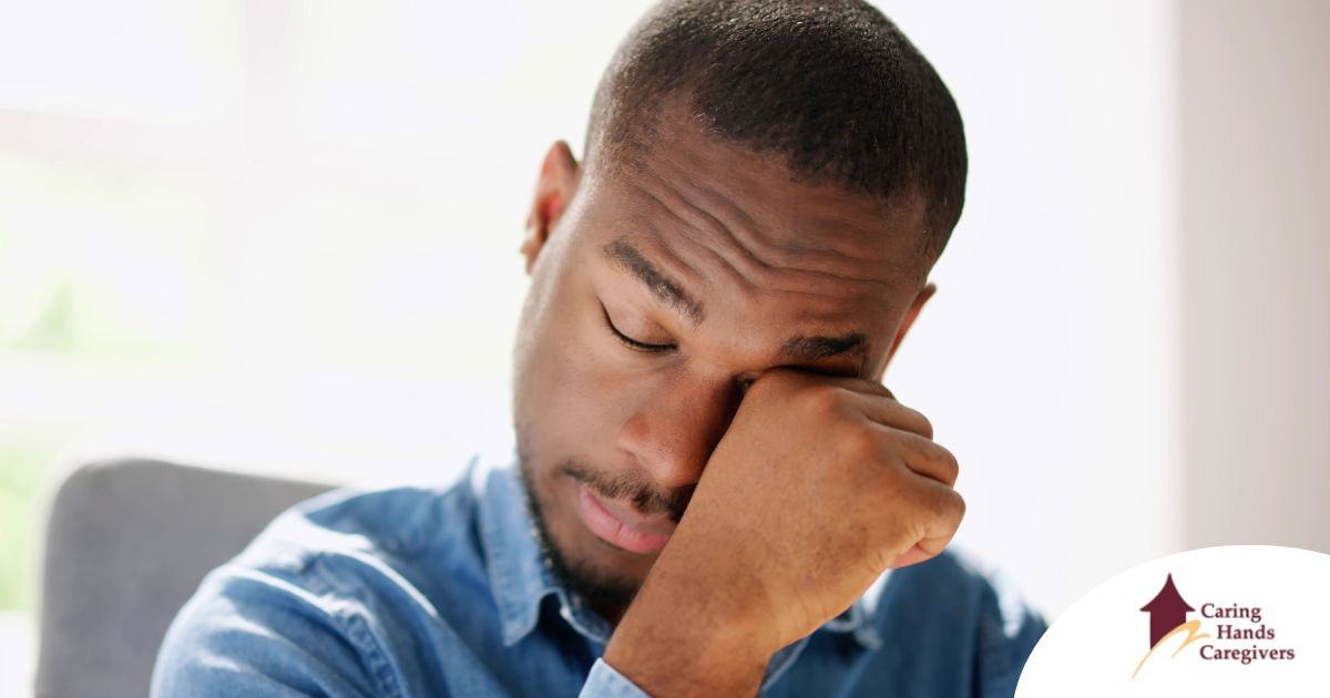 A man tiredly rubs his eyes, representing the exhaustion that can come with family caregiving.